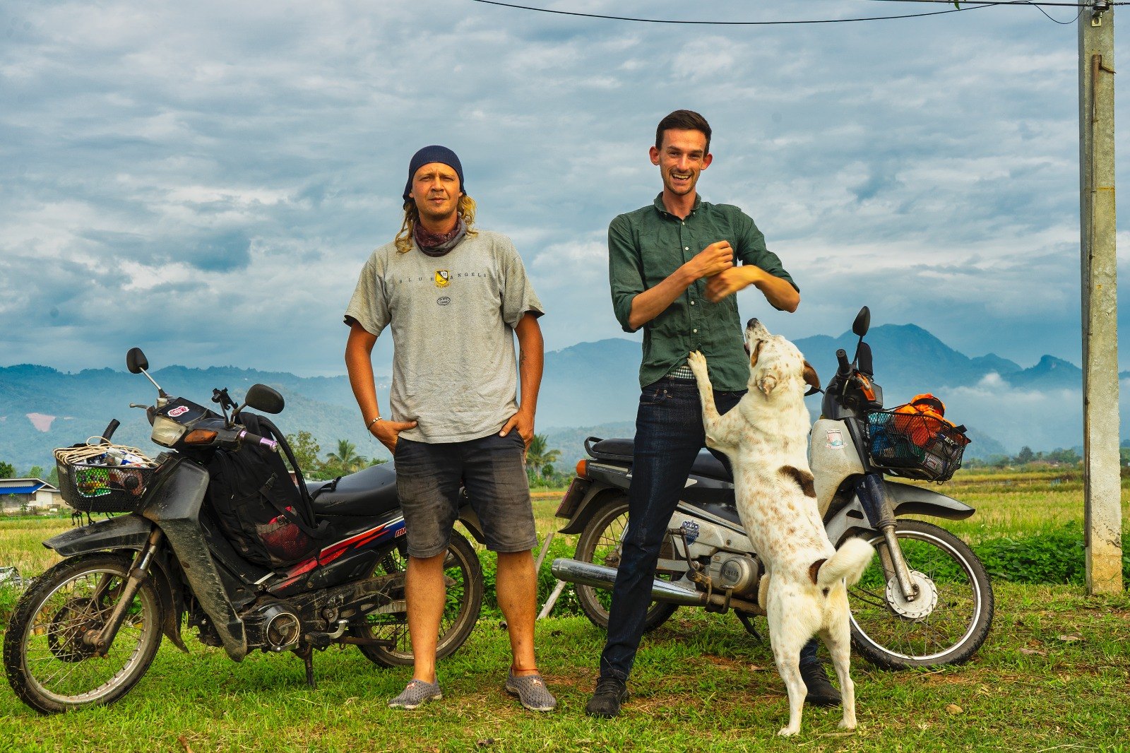 Jack and a friend standing in front of two well-travelled motorbikes, mountains behind
