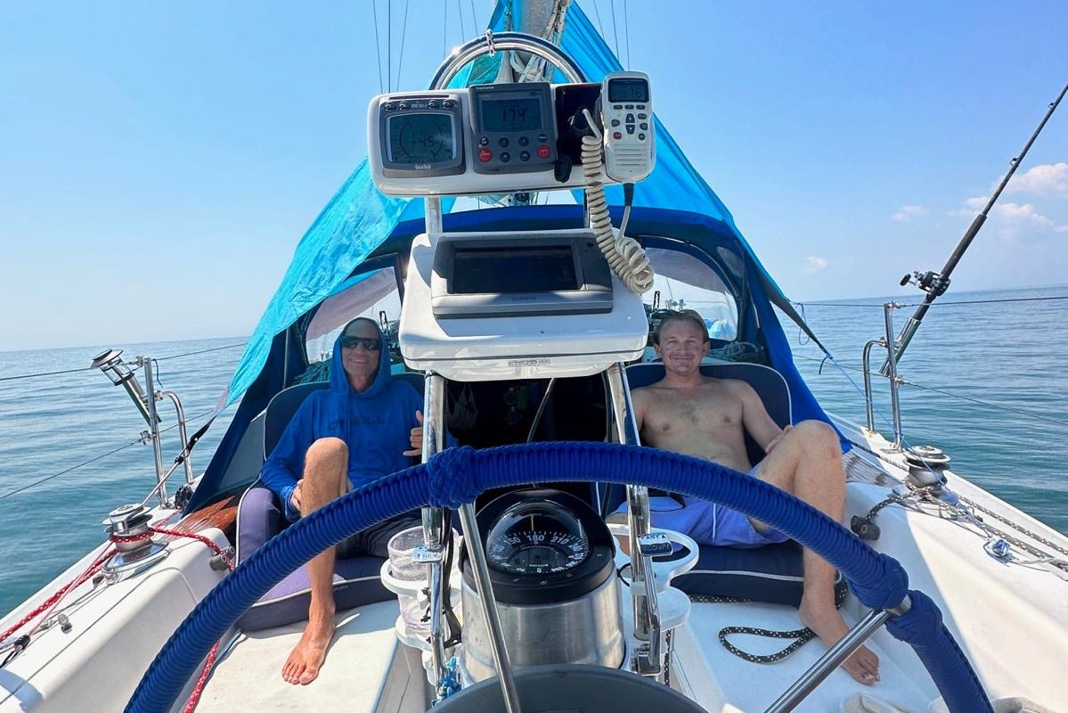 Two crew relaxing in the cockpit of a sailboat behind the wheel, open sea all around